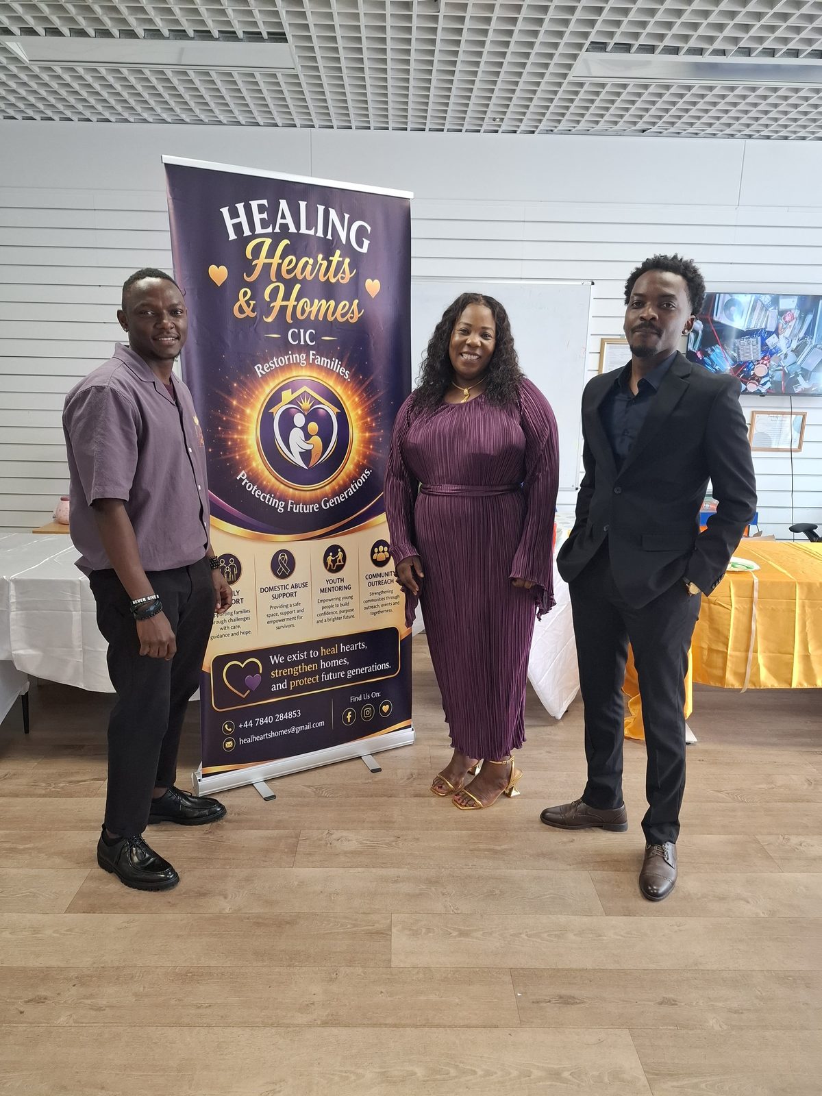 Team members standing beside the Healing Hearts & Homes CIC launch event banner